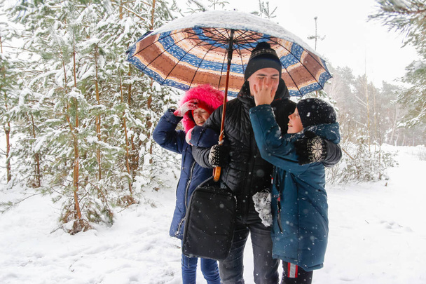 Young man and funny children girl and boy on rural winter snowy background holding umbrella. Happy family, cold weather. Lifestyle. Vacations. Snowy winter, lost in forest. Older brother. Fool. - Foto, Bild