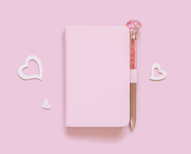 Pink notebook, decorative gemstone pen and hearts on light pink top view. Minimal scene with textbook mockup. Planner cover with place fot text. Valentines, educational and girly concept - Foto, imagen