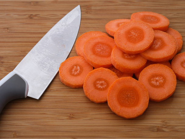 Heap of Orange carrot slices with knife on a wooden cutting board. Close-up - Foto, Imagen