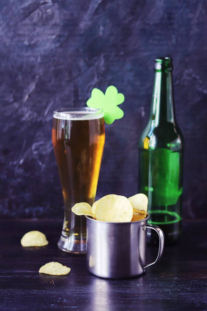 Giorno di Patrick, birra in un bicchiere e una bottiglia, patatine in una tazza di ferro, trifoglio su uno sfondo scuro, festa, congratulazioni, cartolina  - Foto, immagini