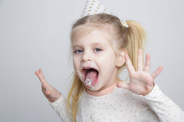 Schattig klein verjaardagsmeisje met kleurrijke suikerhagelslag op lippen en in de mond. Begrip "kinder- en suikerverslaving". - Foto, afbeelding