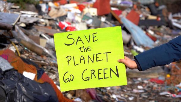 Un enfant écologiste et écologiste de 7 ans tenant une pancarte avec les mots sauver la planète passe au vert, protester contre le changement climatique, le réchauffement climatique et la pollution atmosphérique dans une décharge - Photo, image