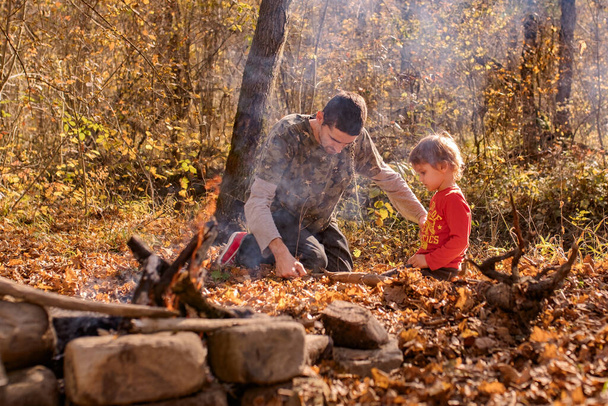 vader en zoon zagen een boomstam met een draadzaag in het kamp herfst, tijd samen doorbrengen - Foto, afbeelding
