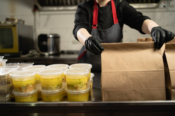 food delivery in the restaurant. Close-up of a hand in gloves wrapping a disposable paper bag. Small business takeaway concept. Copy space. - Photo, image