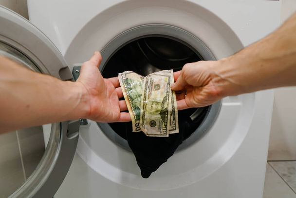 Frustrated man getting out clothes with wet money dollar banknotes from washing machine. - Zdjęcie, obraz