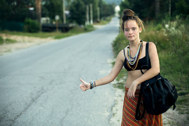 Niedliche Hippie-Tramperin hält ihren Arm hin und stoppt das Auto auf der Straße. - Foto, Bild