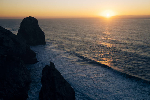 Näkymä kallioille ja pehmeä surffailla Atlantin valtamerellä hämmästyttävä auringonlasku Miradouro da Praia do Caneiro, Portugali.  - Valokuva, kuva