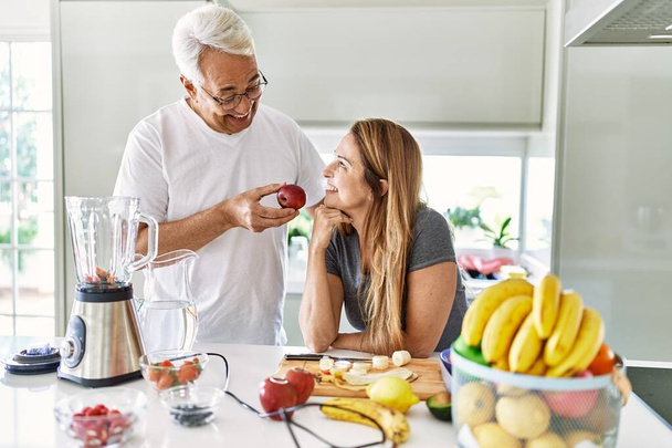 Middle age hispanic couple smiling happy cooking smoothie at the kitchen. - Photo, Image