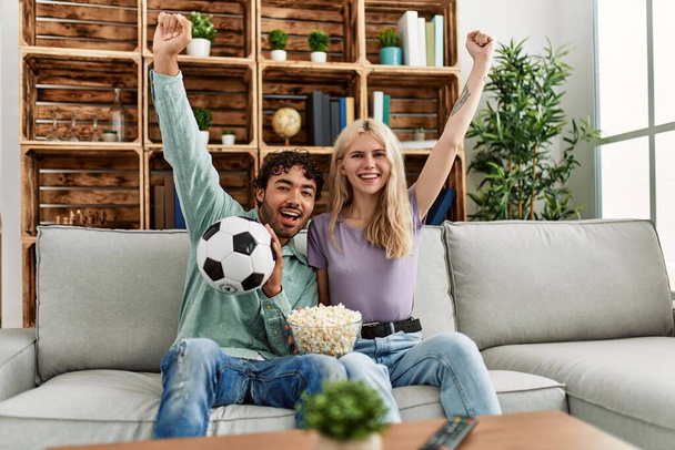 Junges Paar beobachtet Fußballspiel und isst zu Hause Porpcorn. - Foto, Bild