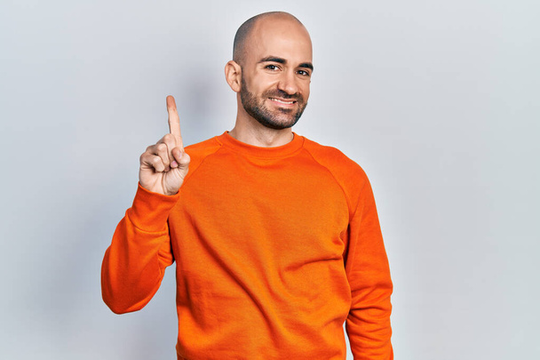 Young bald man wearing casual clothes smiling with an idea or question pointing finger up with happy face, number one  - Valokuva, kuva