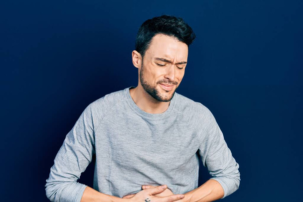 Young hispanic man wearing casual clothes with hand on stomach because indigestion, painful illness feeling unwell. ache concept.  - Photo, Image