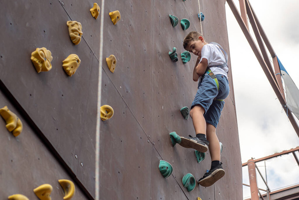 A boy descends on a rope on a climbing wall in a sports park climbing wall. - Фото, изображение
