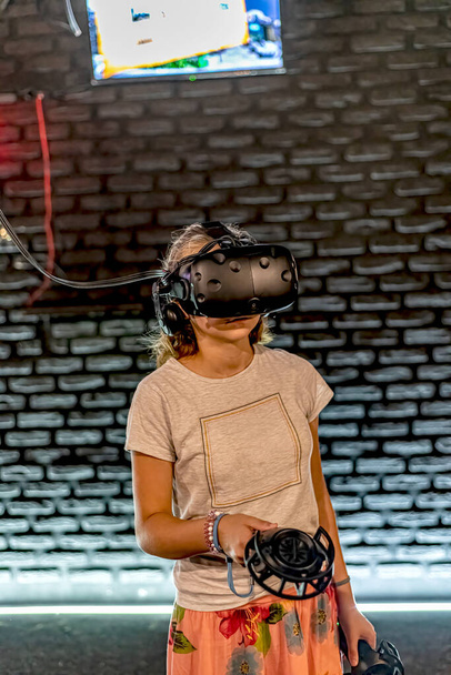 Dívka v helmě VR hraje hry v počítačové místnosti a ovládá joysticky. - Fotografie, Obrázek