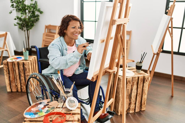 Middle age hispanic disabled artist woman drawing sitting on wheelchair at art studio. - Foto, Bild