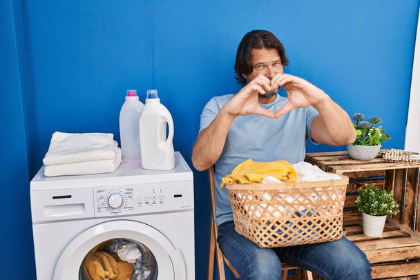 Handsome middle age man waiting for laundry smiling in love doing heart symbol shape with hands. romantic concept.  - Photo, image