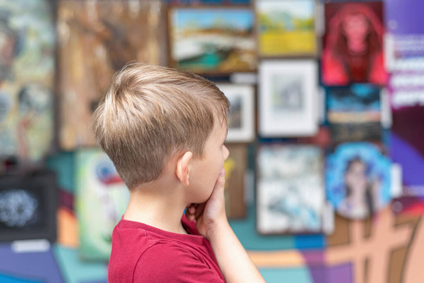 A boy in an art gallery looks at the paintings in the exhibition hall with attention. - Photo, Image