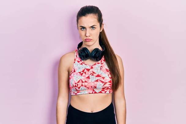Young brunette teenager wearing gym clothes and using headphones depressed and worry for distress, crying angry and afraid. sad expression.  - Foto, Imagen