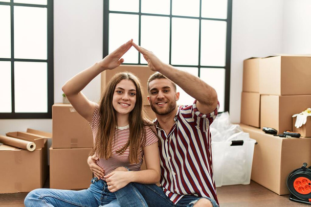 Junges kaukasisches Paar macht Haussymbol mit erhobenen Armen im neuen Zuhause. - Foto, Bild