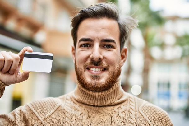 Giovane uomo caucasico sorridente felice con carta di credito in mano alla città. - Foto, immagini