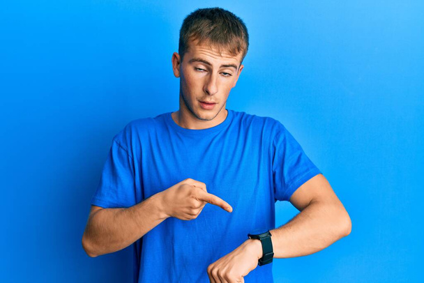 Young caucasian man wearing casual blue t shirt in hurry pointing to watch time, impatience, upset and angry for deadline delay  - Фото, изображение