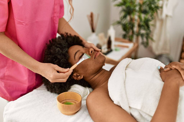 Young african american woman having facial treatment at beauty center - Fotó, kép