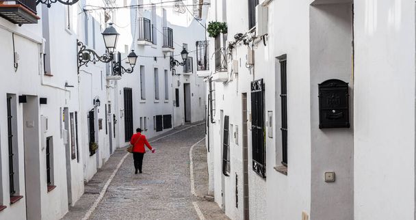 Αγνώριστη γυναίκα με κόκκινο σακάκι περπατά στο δρόμο της παλιάς πόλης της Αλτέας (Αλικάντε, Ισπανία) - Φωτογραφία, εικόνα