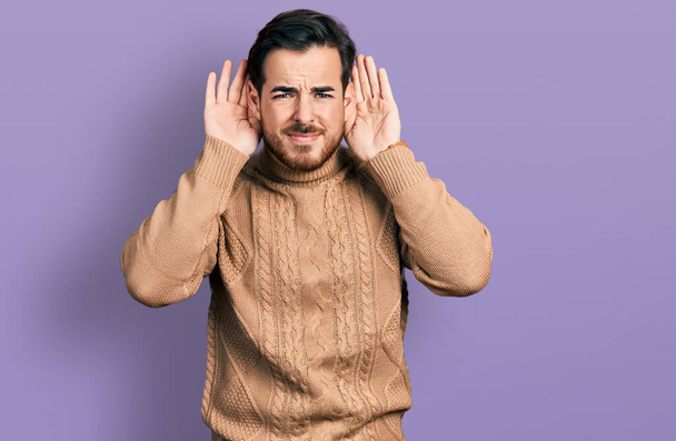 Junger hispanischer Mann in lässiger Kleidung, der versucht, beide Hände am Ohr zu hören, neugierig auf Klatsch. Hörprobleme, Gehörlosigkeit  - Foto, Bild