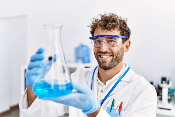 Mladý hispánec muž na sobě vědec uniforma držení zkumavky v laboratoři - Fotografie, Obrázek