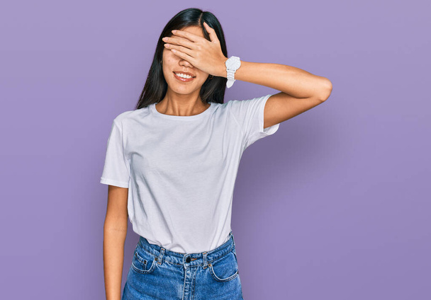 Beautiful young asian woman wearing casual white t shirt smiling and laughing with hand on face covering eyes for surprise. blind concept.  - Foto, Imagem