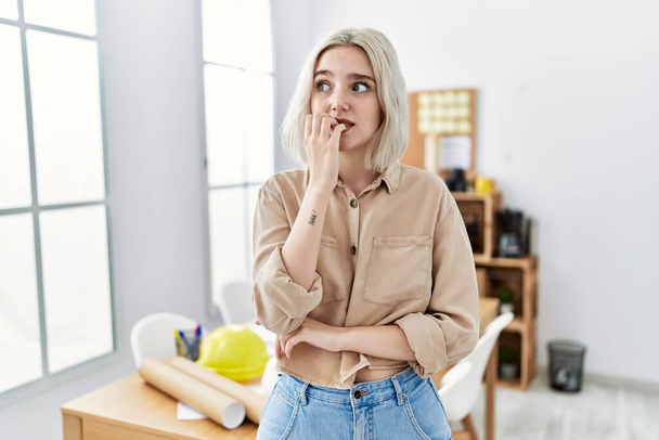 Young beautiful caucasian woman at construction office looking stressed and nervous with hands on mouth biting nails. anxiety problem.  - Photo, image