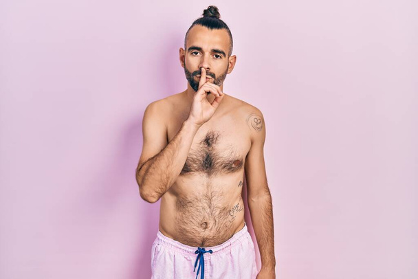 Young hispanic man shirtless wearing swimsuit asking to be quiet with finger on lips. silence and secret concept.  - Fotoğraf, Görsel