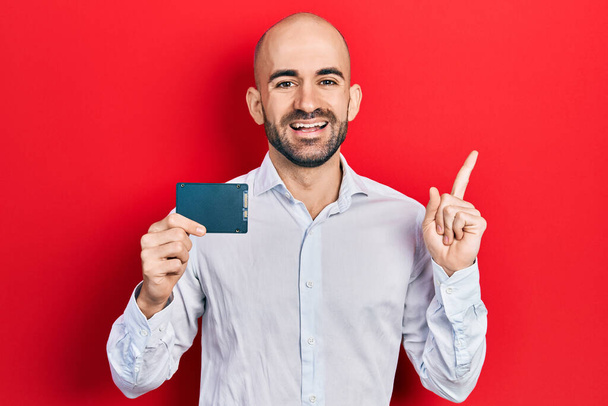 Young bald man holding ssd memory smiling happy pointing with hand and finger to the side  - Photo, image
