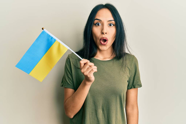 Young hispanic girl wearing ukraine flag scared and amazed with open mouth for surprise, disbelief face  - Foto, Bild