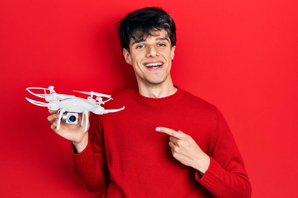 Bonito hipster jovem segurando drone sorrindo feliz apontando com mão e dedo  - Foto, Imagem