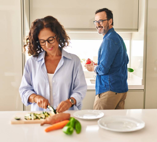 Latynoska para w średnim wieku uśmiecha się pewnie gotując w kuchni - Zdjęcie, obraz