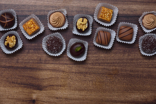 Various chocolate pralines lie at the top on a wooden background - Fotó, kép