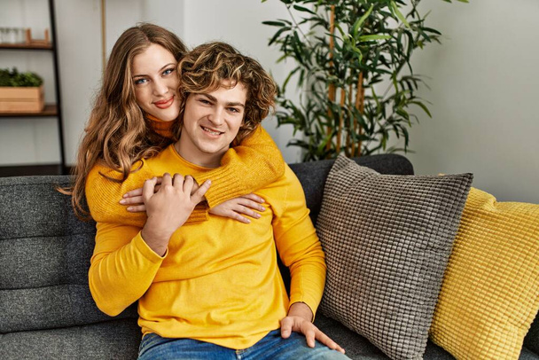 Jovem casal caucasiano sorrindo confiante abraçando uns aos outros em casa - Foto, Imagem
