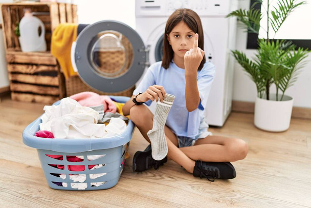 Young hispanic girl doing laundry holding socks showing middle finger, impolite and rude fuck off expression  - Fotografie, Obrázek
