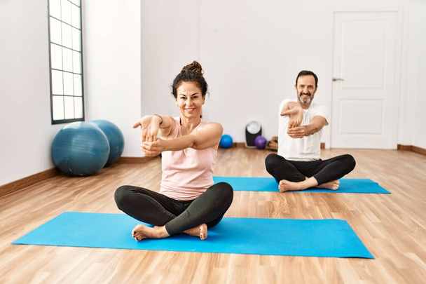 Volwassen Latijns-Amerikaanse echtpaar doen oefeningen en stretching in yoga kamer. Twee volwassen mensen doen pilates en flexibiliteit workout - Foto, afbeelding