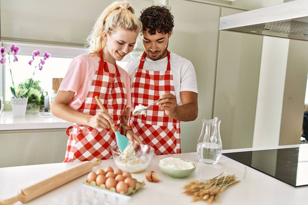 Молода пара посміхається щасливим змішуванням інгредієнтів, щоб зробити тісто для домашнього хліба на кухні
. - Фото, зображення