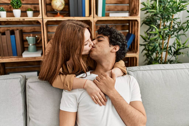 Молодая пара целуется и обнимается сидя дома на диване. - Фото, изображение