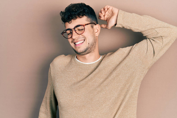Young hispanic man wearing casual clothes and glasses stretching back, tired and relaxed, sleepy and yawning for early morning  - Фото, зображення