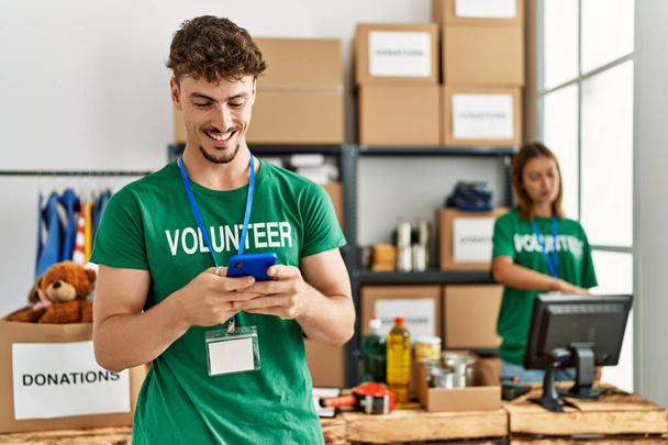 Een jong Spaans vrijwilligerspaar dat werkt bij een liefdadigheidscentrum. Man glimlachend blij met smartphone. - Foto, afbeelding