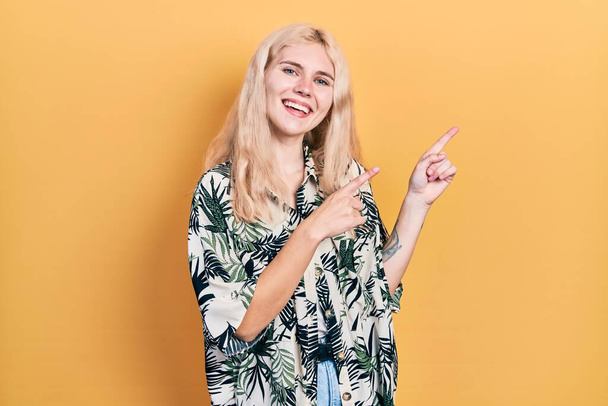 Beautiful caucasian woman with blond hair wearing tropical shirt smiling and looking at the camera pointing with two hands and fingers to the side.  - Fotó, kép