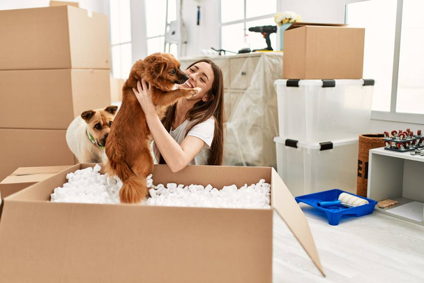 Junge hispanische Frau hält Hund aus Paket auf dem Boden im neuen Zuhause - Foto, Bild