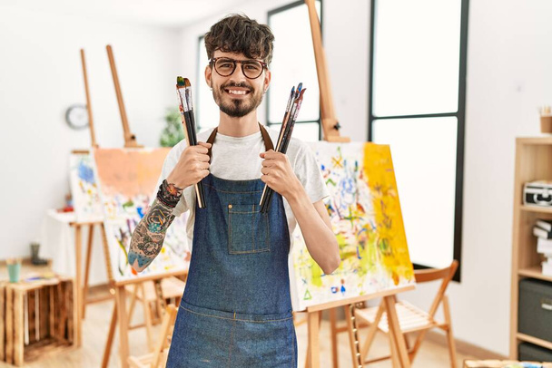 Молодий іспаномовний художник, посміхаючись, щасливий тримає пензлі в художній студії
. - Фото, зображення