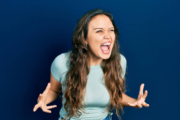 Young hispanic girl wearing casual clothes crazy and mad shouting and yelling with aggressive expression and arms raised. frustration concept.  - Foto, Imagen