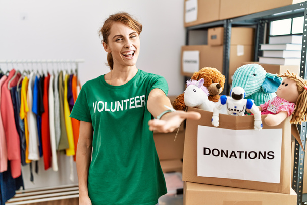 Beautiful caucasian woman wearing volunteer t shirt at donations stand smiling friendly offering handshake as greeting and welcoming. successful business.  - Foto, Imagem