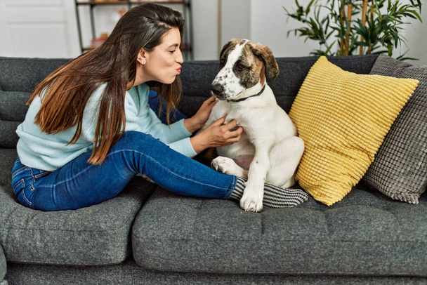 Junge Frau umarmt Hund, der zu Hause auf Sofa sitzt - Foto, Bild
