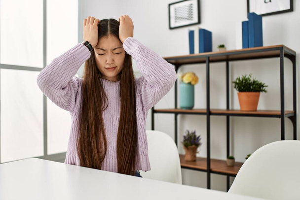Young chinese girl wearing casual clothes sitting on the table at home suffering from headache desperate and stressed because pain and migraine. hands on head.  - Φωτογραφία, εικόνα